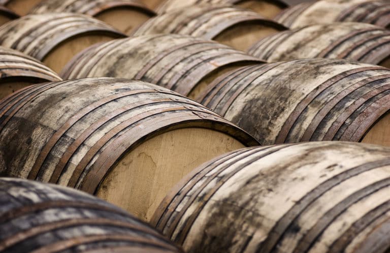 Im Bild sind Whisky-Fässer zu sehen, die in Reihe auf dem Boden liegen als Titelbild zur Folge 10 – Welcome to the noble Scotch Society