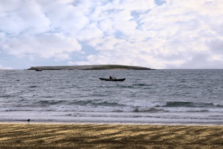 Ein einzelner Ruderer in einem alten traditionellen irischen Curragh-Boot in der Nähe eines Strandes an der Westküste Irlands. Das Titelbild zur Folge 16 – Whisky in a Nutshell, Steamship ahoi!