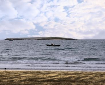 A single rower in an ancient traditional irish curragh boat near a beach on the west coast of ireland