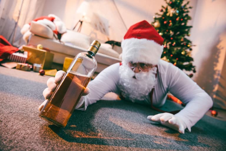Ein Weihnachtsmann der mit einer angeborchenen Flasche Whisky auf dem Boden eines Wohnzimmers liegt. Das Titelbild zur Folge 19 – Merry Blue Cokemas