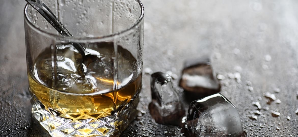 Whiskey in a glass and pieces of ice on a wood