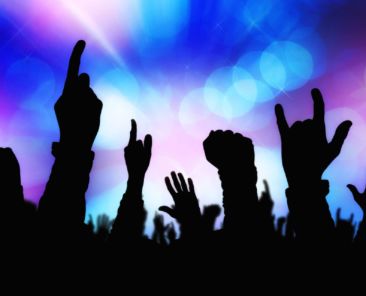 Silhouettes of concert crowd hands supporting band performing live music on stage, young people on rock gig enjoying.