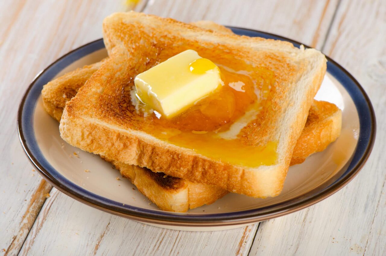 Zwei Toastscheiben auf einem Teller der auf einem Holzstisch steht. Auf dem Toast zerläuft Butter. Das Titelbild zur Folge 39 – Snacktime: Whisky auf Toast