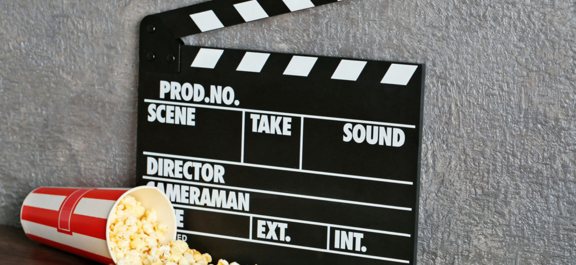 Movie clapper and popcorn against grey wall background