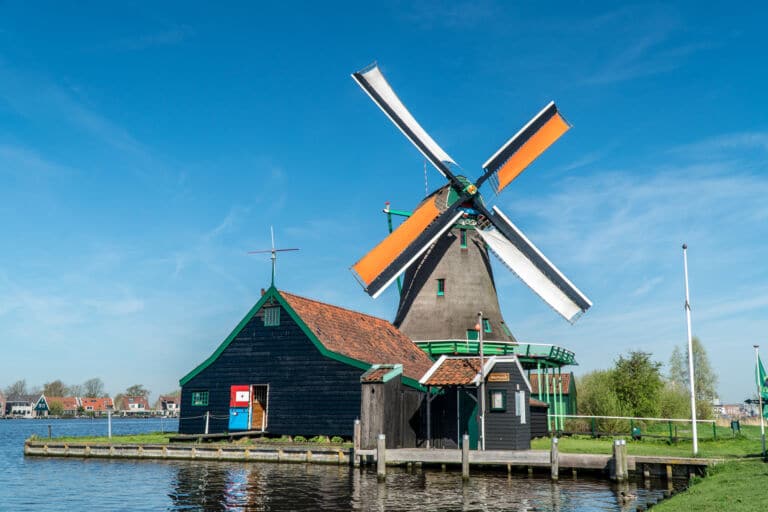 Eine Windmühle über einem See in den Niederlanden als Titelbild zur Folge 76 – Oranje tamtamje van de paarden en windmolens