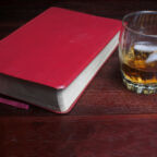 A glass of bourbon on the rocks next to a bible.