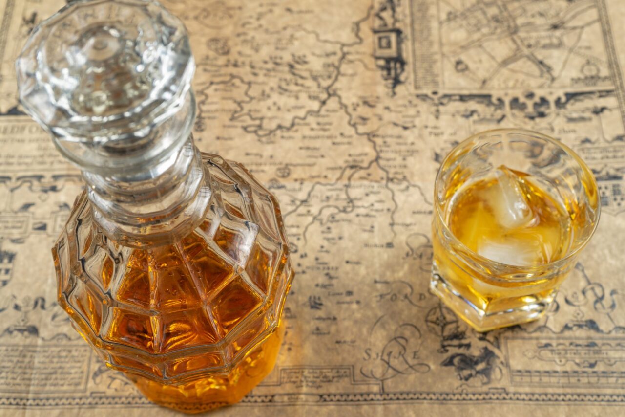 Ein Glas Dekanter mit einem gefüllten Glas auf einer Landkarte. Das Titelbild zur Folge 110 – Geschmacklich auf Weltreise?