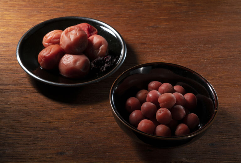 Zwei Schalen mit japanischen Umeboshi-Pflaumen auf Holz, fotografiert als Stillleben. Titelbild zur Folge 122 – Plum Plum Whisky.