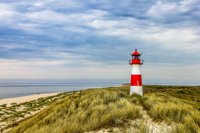Leuchtturm in Dünenlandschaft mit Meer im Hintergrund – Folge 162