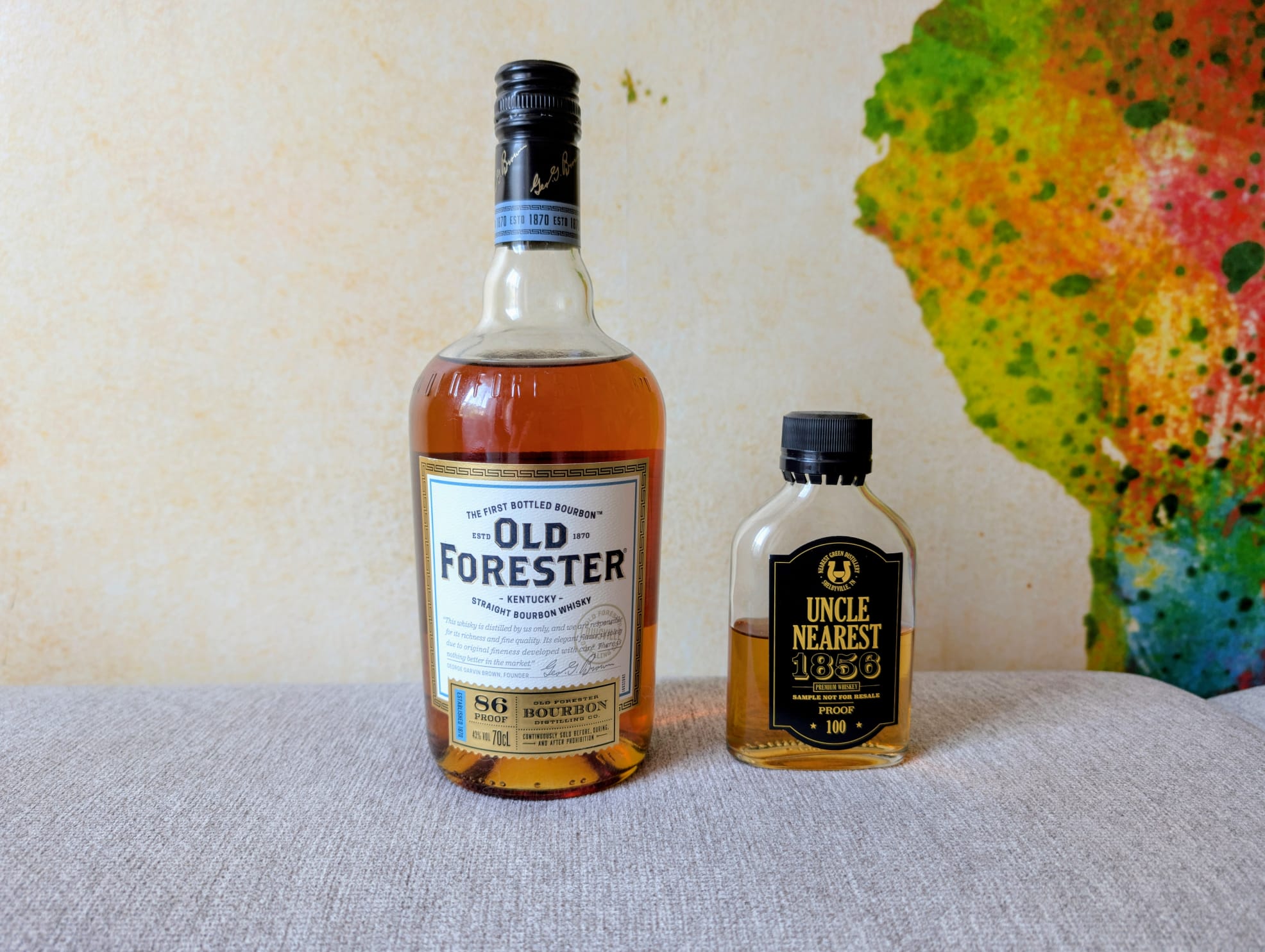 Old Forester 86 Proof Bourbon und Uncle Nearest 1856 Premium Whiskey stehen nebeneinander vor einer bunten Wand – Grab The Glass Folge 217