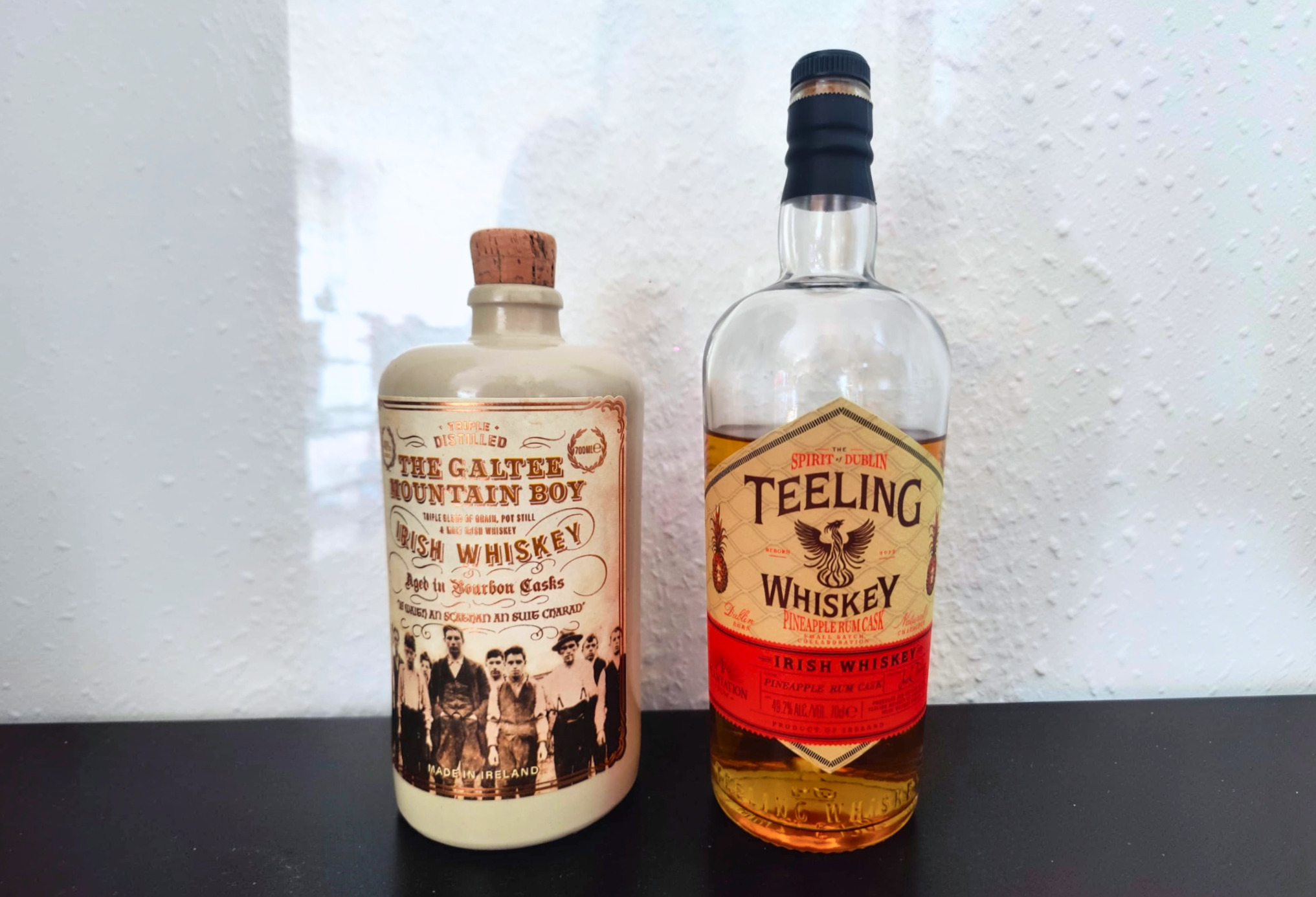 The Galtee Mountain Boy und Teeling Pineapple Rum Cask stehen nebeneinander auf einem schwarzen Tisch.