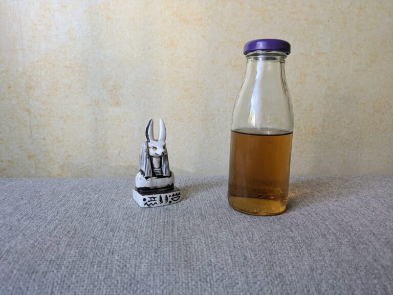 Pharaohs Whisky Style in einer Glasflasche neben einer kleinen Anubis-Figur auf grauem Untergrund.